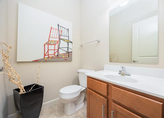 A bathroom with a toilet, sink, and a painting of a chair.