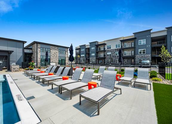 A poolside area with sun loungers and a row of apartment buildings in the background.