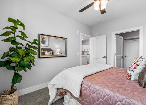 A bedroom with a bed, a ceiling fan, and a potted plant.