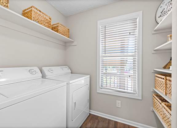A laundry room with a washer and dryer and a window with blinds.