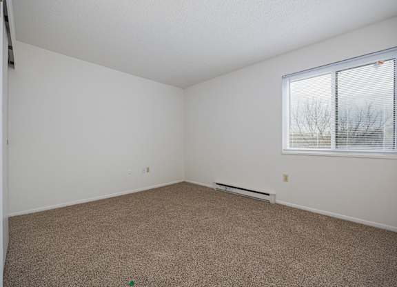A room with a carpeted floor and a window with blinds.