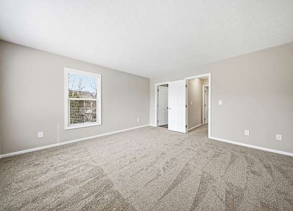 A large, empty room with a carpeted floor and a window with blinds.