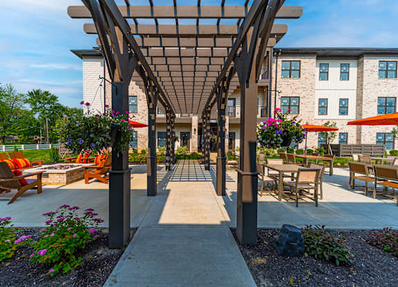 A patio with a pergola and chairs is surrounded by a building.