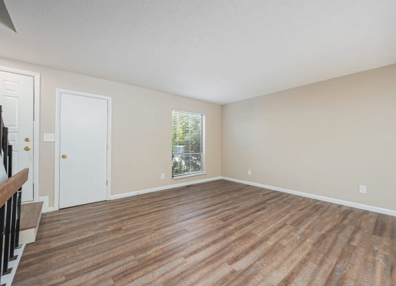 an empty living room with wood flooring and a window