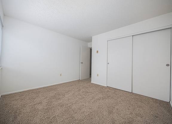 A room with white walls and carpeted floor with a window on the left.
