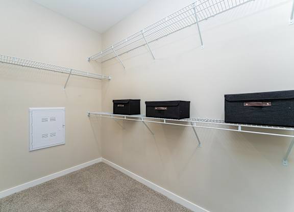 A room with a white ceiling, beige walls, and a carpeted floor with three black storage boxes on shelves.