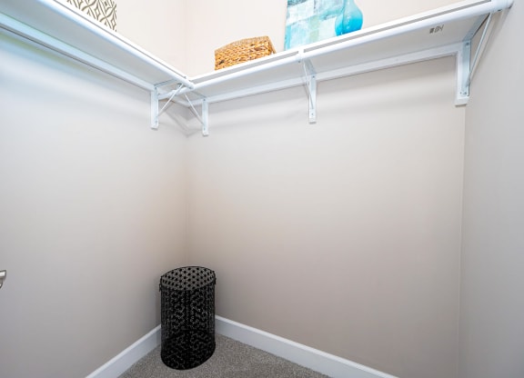 a walk in closet with a white wall and a small stool