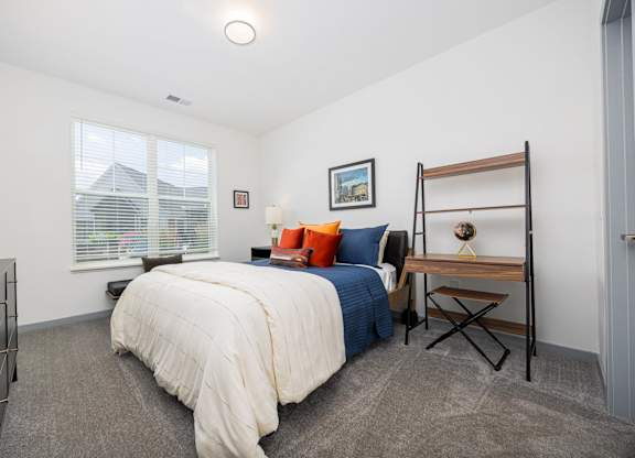 A bedroom with a bed, a desk, and a window.