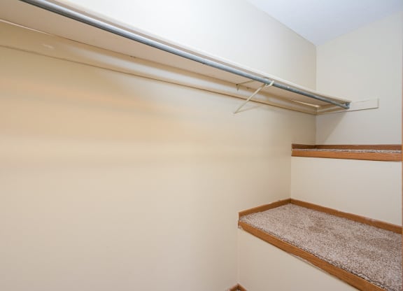 a walk in closet with a white wall and a shelf on the wall