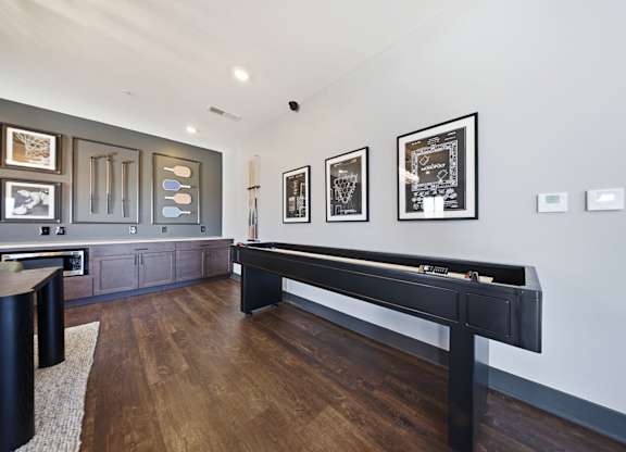 A pool table in a room with a wooden floor and framed pictures on the wall.