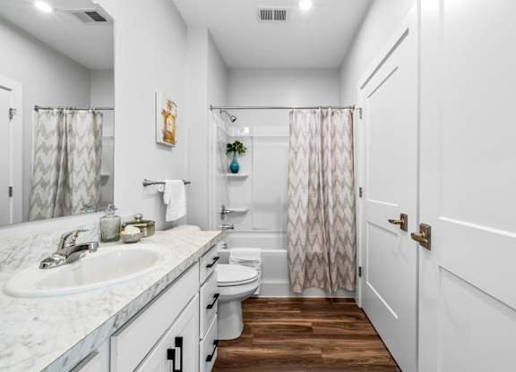 A white bathroom with a marble counter top and a wooden floor.