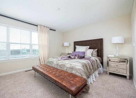 A bedroom with a bed, nightstand, and window with blinds.