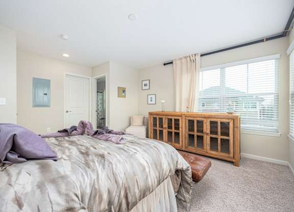 A bedroom with a bed, a window with blinds, and a wooden cabinet.