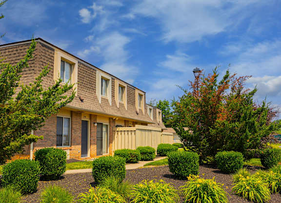 A house with a brown roof and a grey door surrounded by bushes and trees.