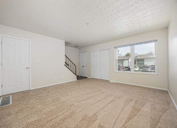A room with a carpeted floor and a window showing a view of other buildings.