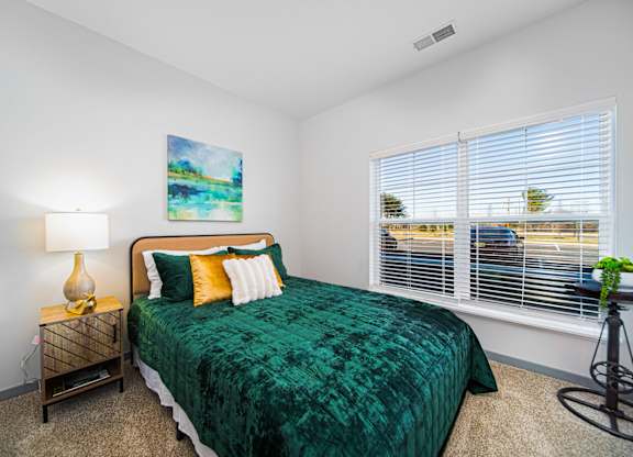 A bedroom with a green bedspread and a painting on the wall.