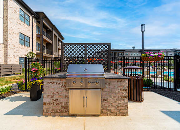 A stone BBQ grill is in the middle of a concrete patio.