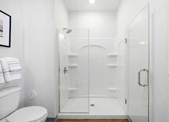 A white bathroom with a toilet, a glass shower door, and a white towel.