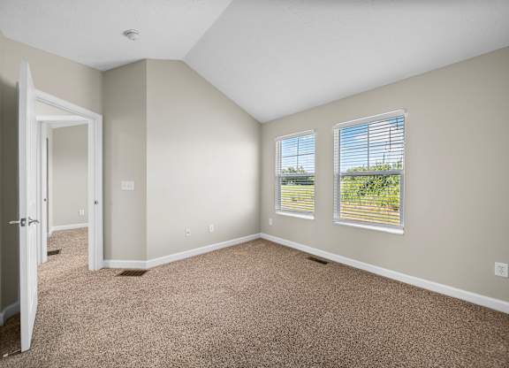 A room with carpeted floor and two windows.