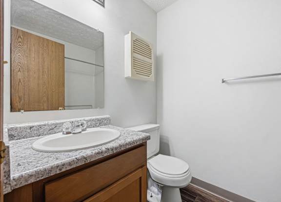 A bathroom with a toilet, sink, mirror, and a towel bar.