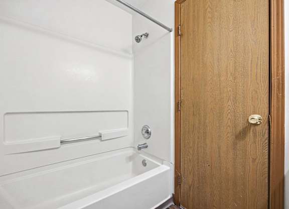 A white bathtub with a shower head and a wooden door.