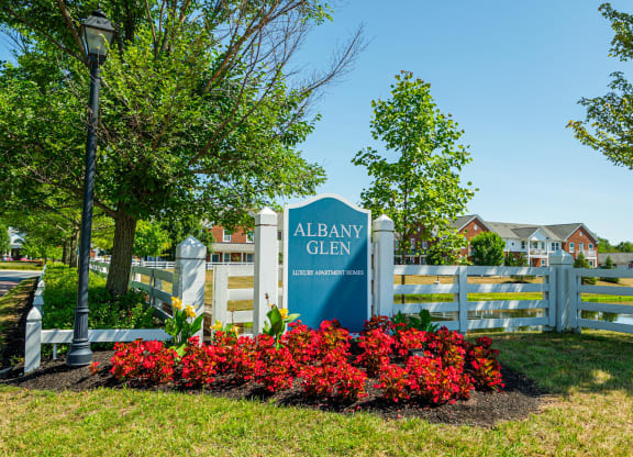 a sign for albany glen in front of a fence and red flowers