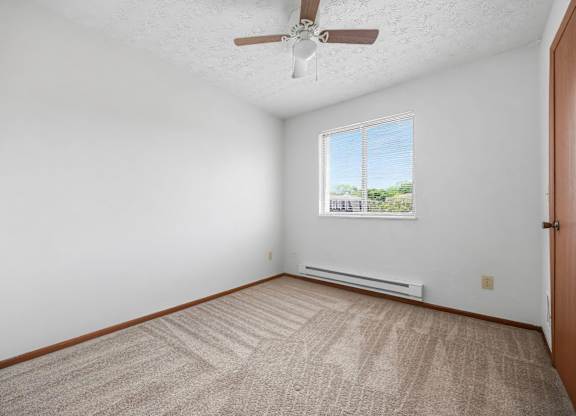 A room with a ceiling fan and a window with a view of trees and a fence outside.