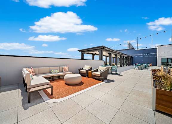 A rooftop patio with a white couch, a brown rug, and a wooden table.