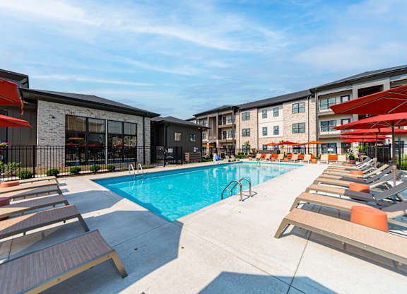 A swimming pool surrounded by sun loungers and apartment buildings.