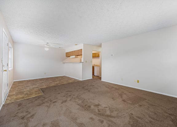 an empty living room with carpet and a kitchen