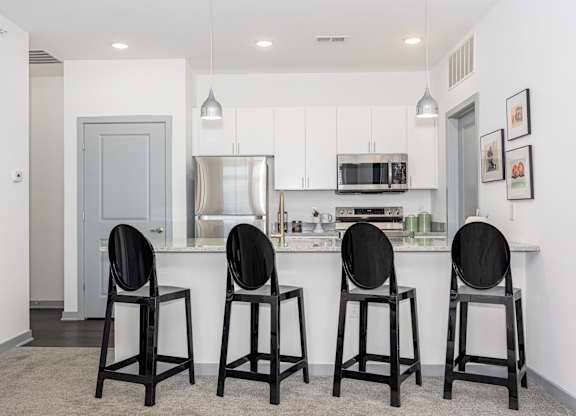 A kitchen with white cabinets and a bar area with four black chairs.