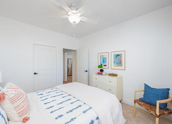 A bedroom with a bed, pillows, a ceiling fan, and a chair.