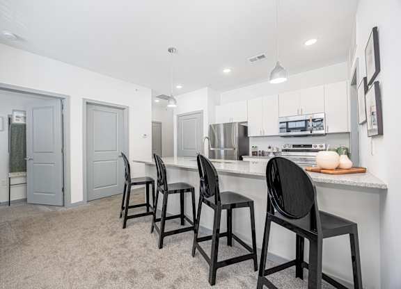 A kitchen with white cabinets and black chairs.