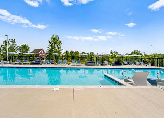 A large swimming pool with lounge chairs and a fence in the background.
