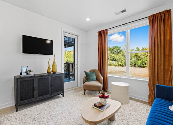 A living room with a blue sofa, a wooden coffee table, a flat screen TV, and a sliding glass door leading to a balcony.