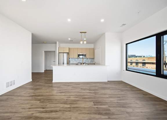 A spacious room with wooden flooring and a large window overlooking a cityscape.