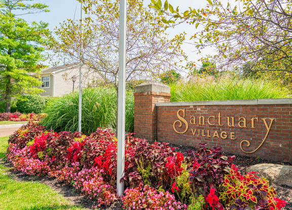 a sign for sanctuary village in front of a brick wall and flowers