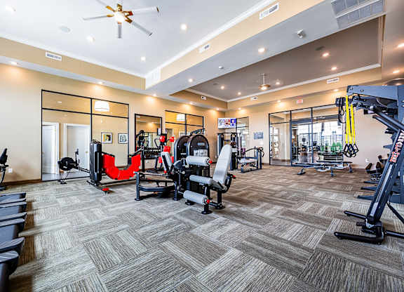 A gym with a variety of equipment including treadmills, weights, and a fan.