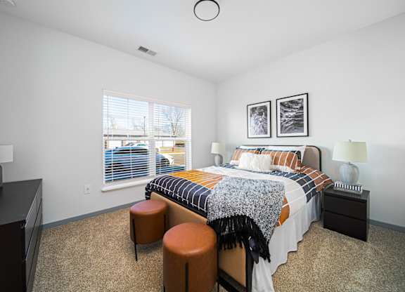 A bedroom with a bed, nightstand, and two stools.