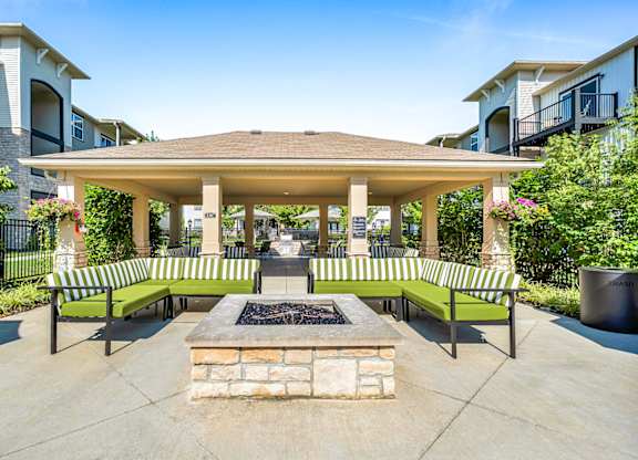 A gazebo with a fire pit in the middle of a courtyard surrounded by benches.