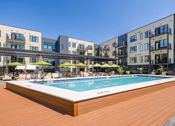 A pool surrounded by wooden deck and buildings.