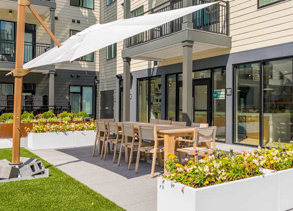 A patio with a white umbrella and wooden chairs.