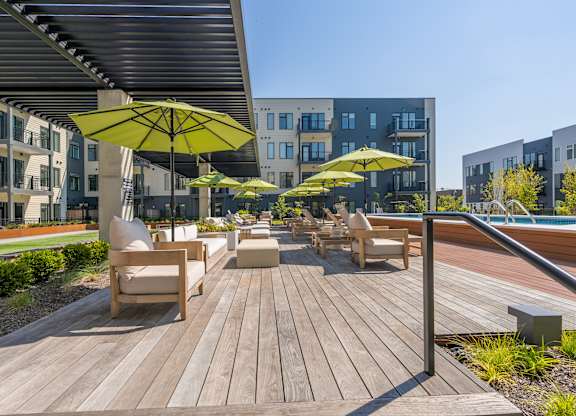 A wooden deck with chairs and umbrellas in front of a building.