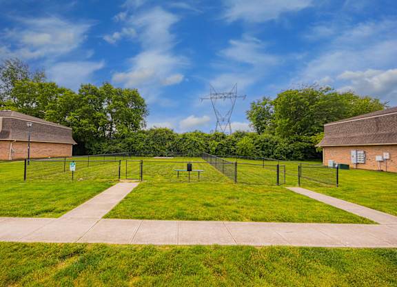 A grassy field with a fence and two buildings in the background.