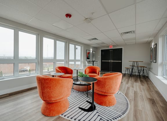 a lounge area with orange chairs and a black and white rug