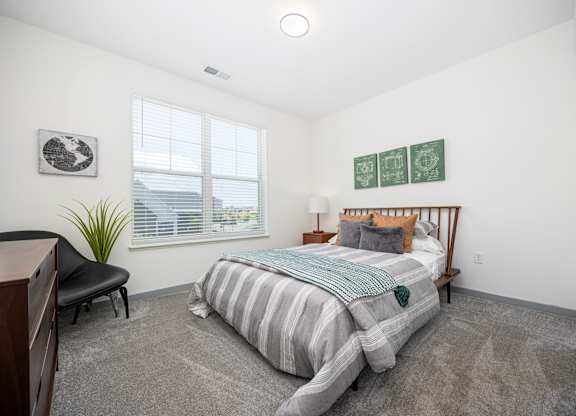 A bedroom with a bed, chair, and a plant.