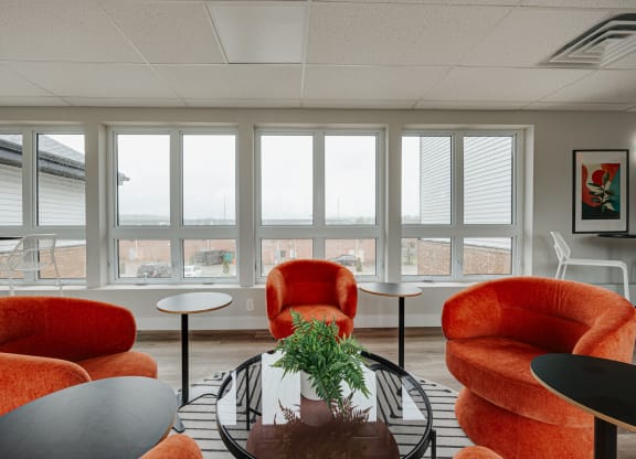 a living room with orange chairs and a table and windows