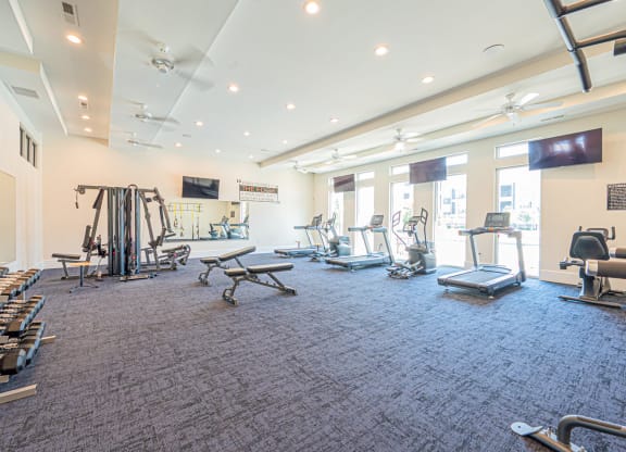 a gym with weights and cardio equipment in a building with windows