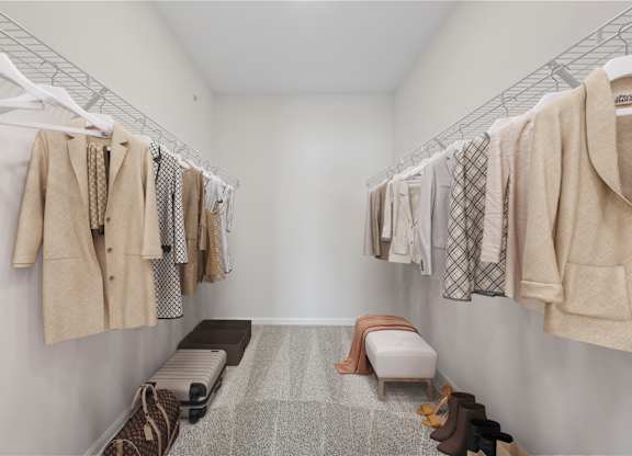 A walk in closet with clothes hanging and a bench.