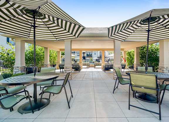 A patio with tables and chairs under striped umbrellas.